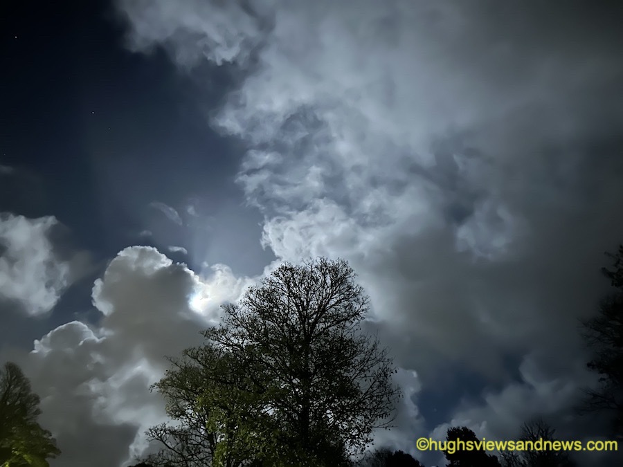 Photo of the moon behind clouds and stars in the sky