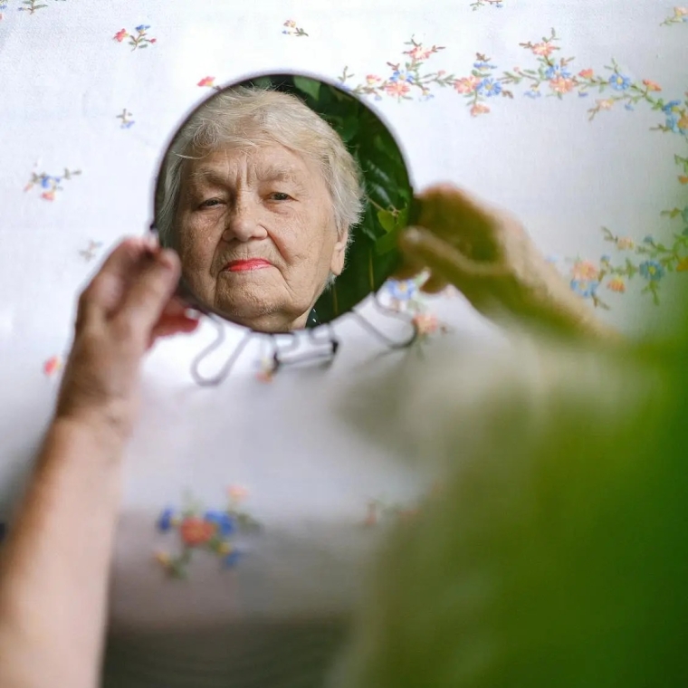 Image of an elderly woman looking at her reflection in a mirror.